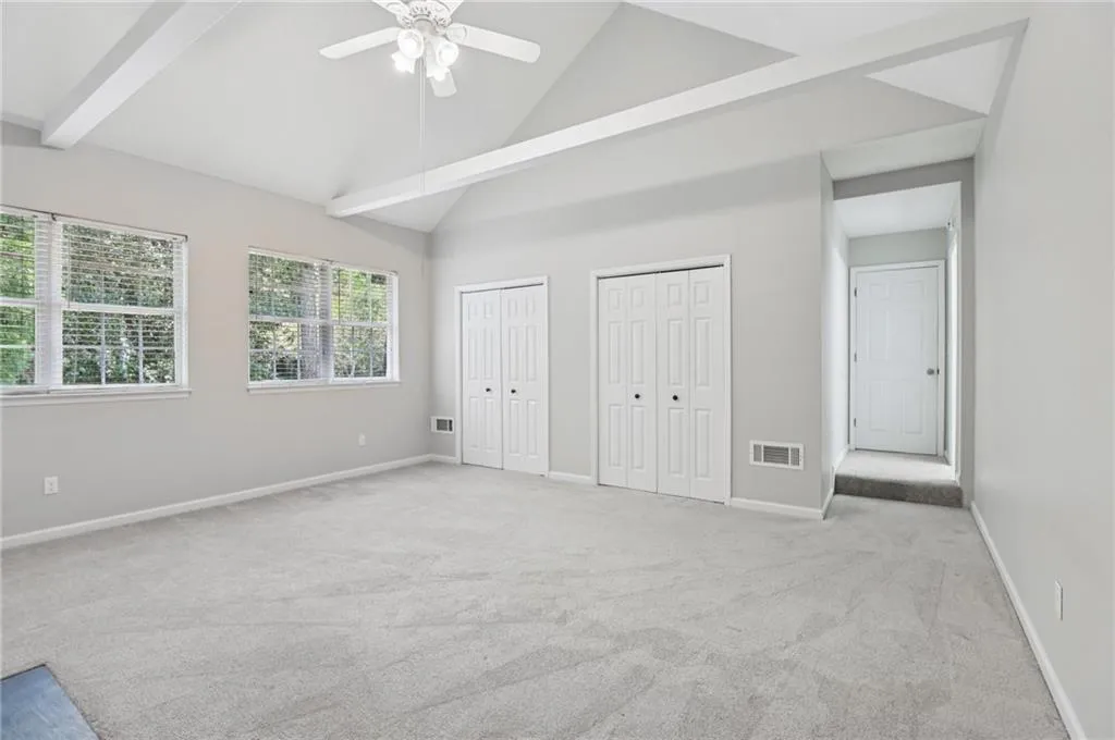 Unfurnished bedroom featuring carpet, two closets, high vaulted ceiling, a ceiling fan, and beamed ceiling