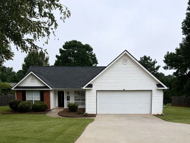 White siding exterior with a dark shingle roof, attached garage, and a concrete driveway