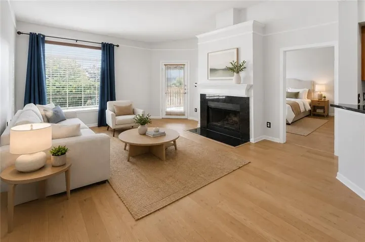 Open concept living area featuring wood-finish flooring and a stone fireplace with a contrasting mantel. Virtually Staged.