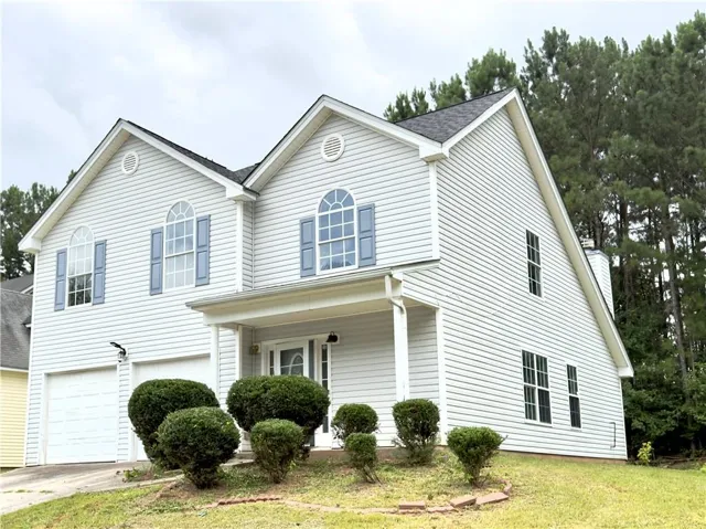 Two-story residence featuring light-colored siding, a covered front porch, and a two-car garage