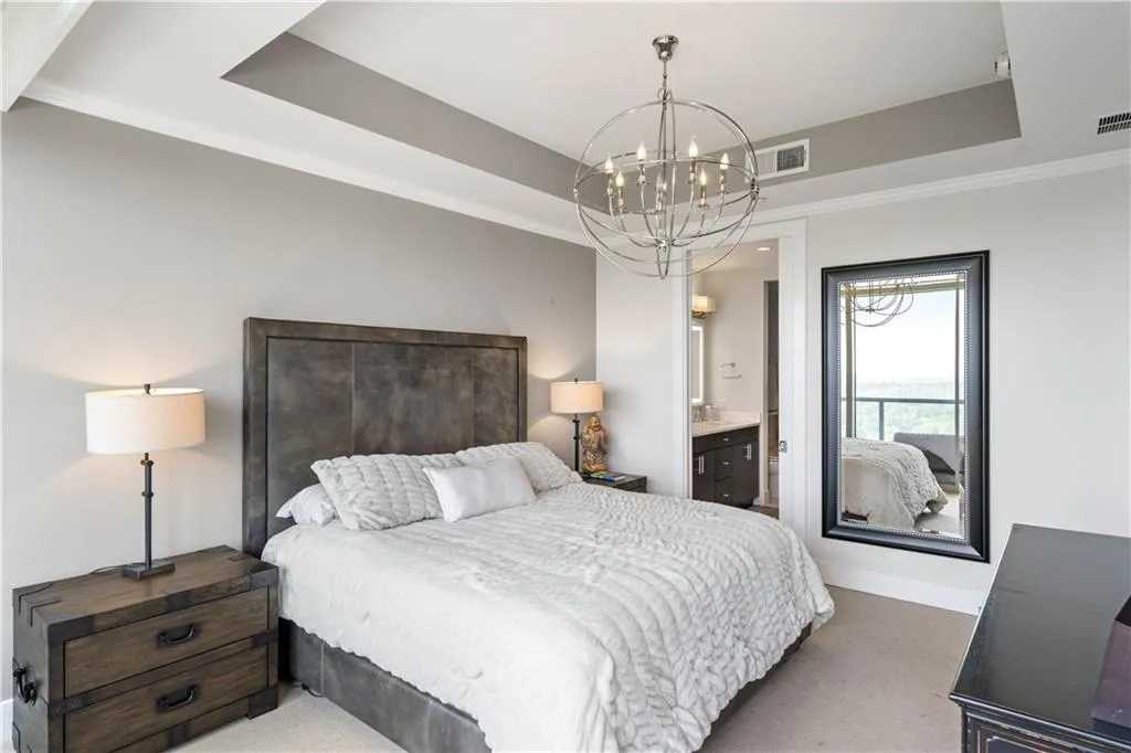 Bedroom with a tray ceiling, crown molding, carpet floors, ensuite bathroom, and a chandelier