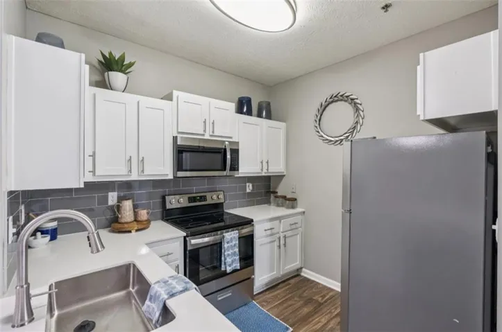 Kitchen featuring white shaker-style cabinetry, stainless steel appliances, a subway tile backsplash, white countertops, and wood-finish flooring