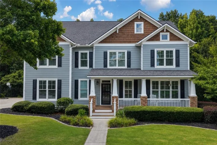 Two-story residence featuring cedar shake and siding, a covered front porch with white columns, dark shutters, and a concrete walkway