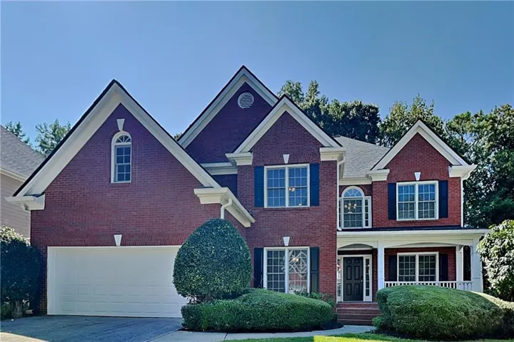 Brick exterior featuring a covered porch, white columns, and a two-car garage