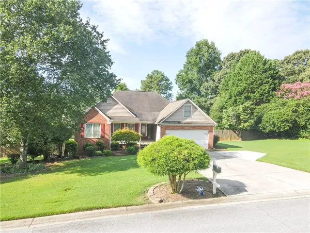 Brick Colonial home set on expansive manicured grounds featuring mature landscaping, circular driveway, two-car garage, and lush tree-lined perimeter