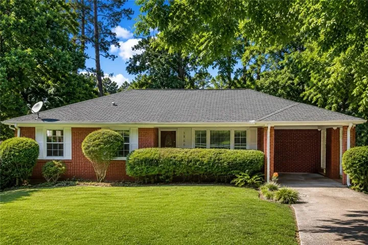 Brick ranch home featuring a dark shingle roof, white window shutters, a covered carport, and a concrete driveway