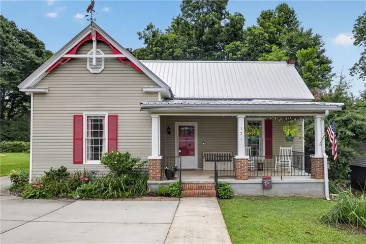 Exterior facade featuring light gray siding, a metal roof, and a covered front porch