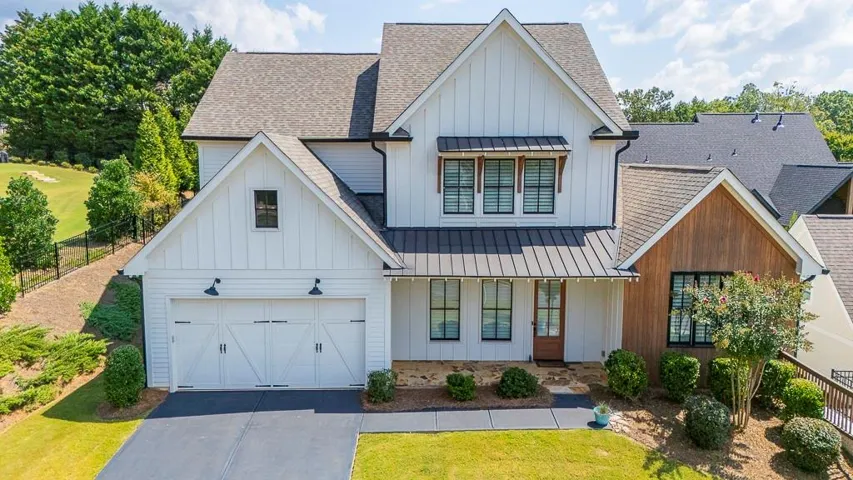 Modern farmhouse exterior with white board-and-batten siding, a dark metal roof accent, a two-car garage with barn-style doors, and dark-framed windows
