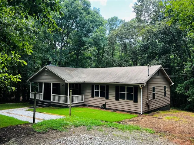 Single-story residence featuring horizontal siding, multiple windows with dark shutters, and a covered front porch with white railings