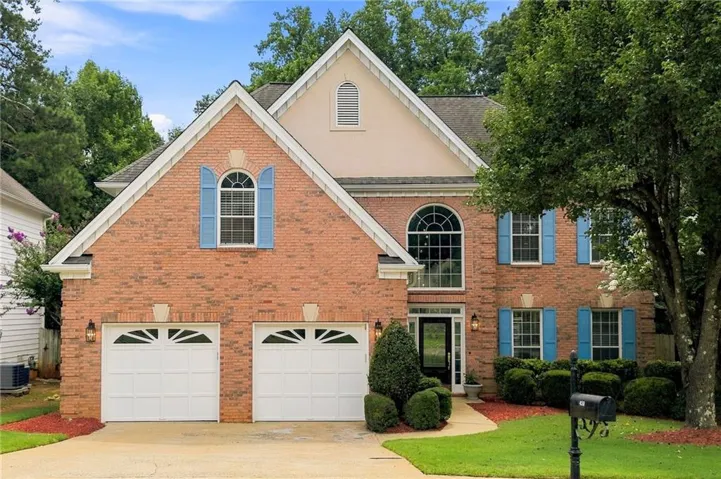 Brick exterior with a prominent arched window, two-car garage, and established landscaping
