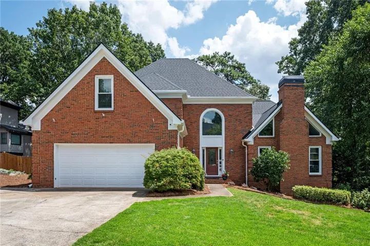 Brick exterior with white trim, arched window feature, attached two-car garage, and a prominent brick chimney