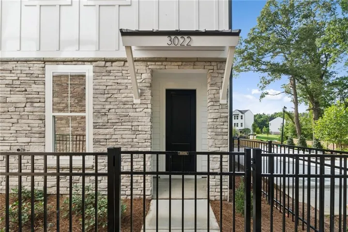 Modern facade featuring white board and batten siding, stacked stone veneer, a covered entry with a black door, and a black metal fence