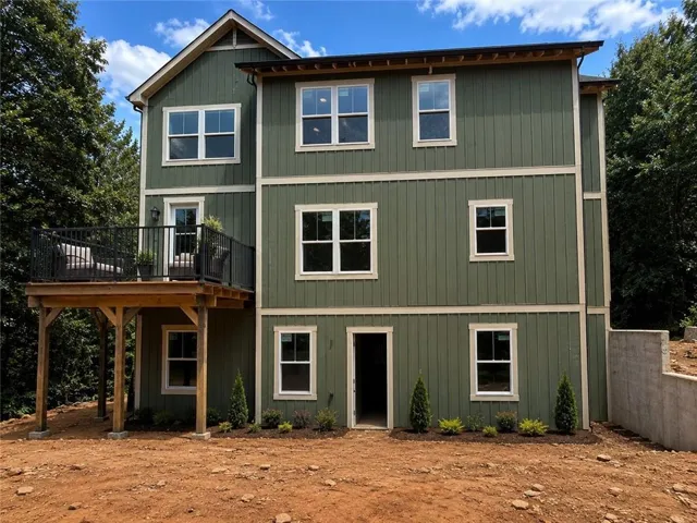 Multi-story exterior featuring board and batten siding, multiple windows, a second-story deck with a black metal railing, and an exposed concrete retaining wall
