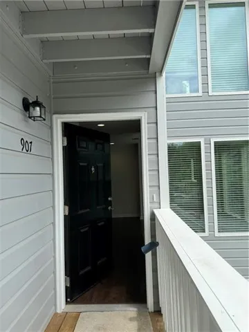 Exterior entrance featuring gray siding, a black paneled front door, an overhead porch light fixture, and a white wood railing