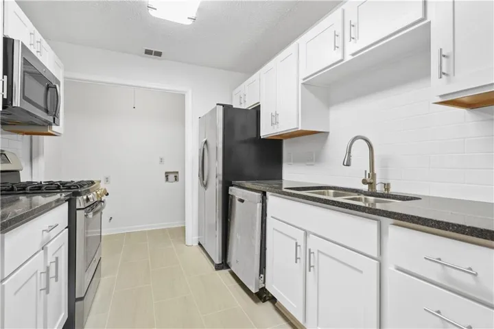 Kitchen featuring white cabinetry, dark speckled countertops, and stainless steel appliances