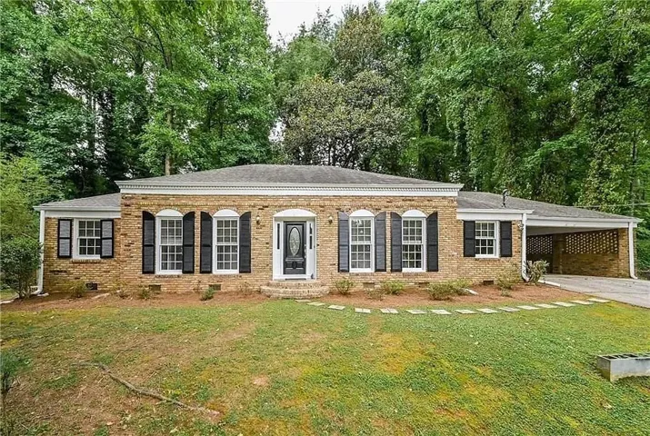 Brick exterior featuring a portico entry with a dark-paneled door, decorative black shutters, multi-pane windows, and a covered carport with a brick privacy screen