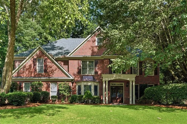 Traditional brick exterior featuring a prominent two-story entry portico with columns, a bay window, and a gabled roofline