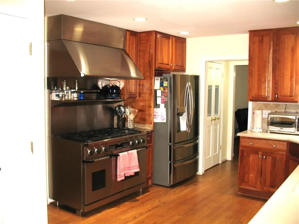 Kitchen with appliances with stainless steel finishes, wall chimney range hood, dark wood-style floors, light countertops, and backsplash