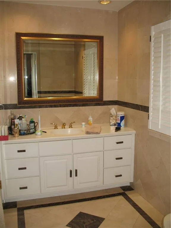 Bathroom featuring inlaid floor details, tile walls, vanity, backsplash, and light tile patterned floors