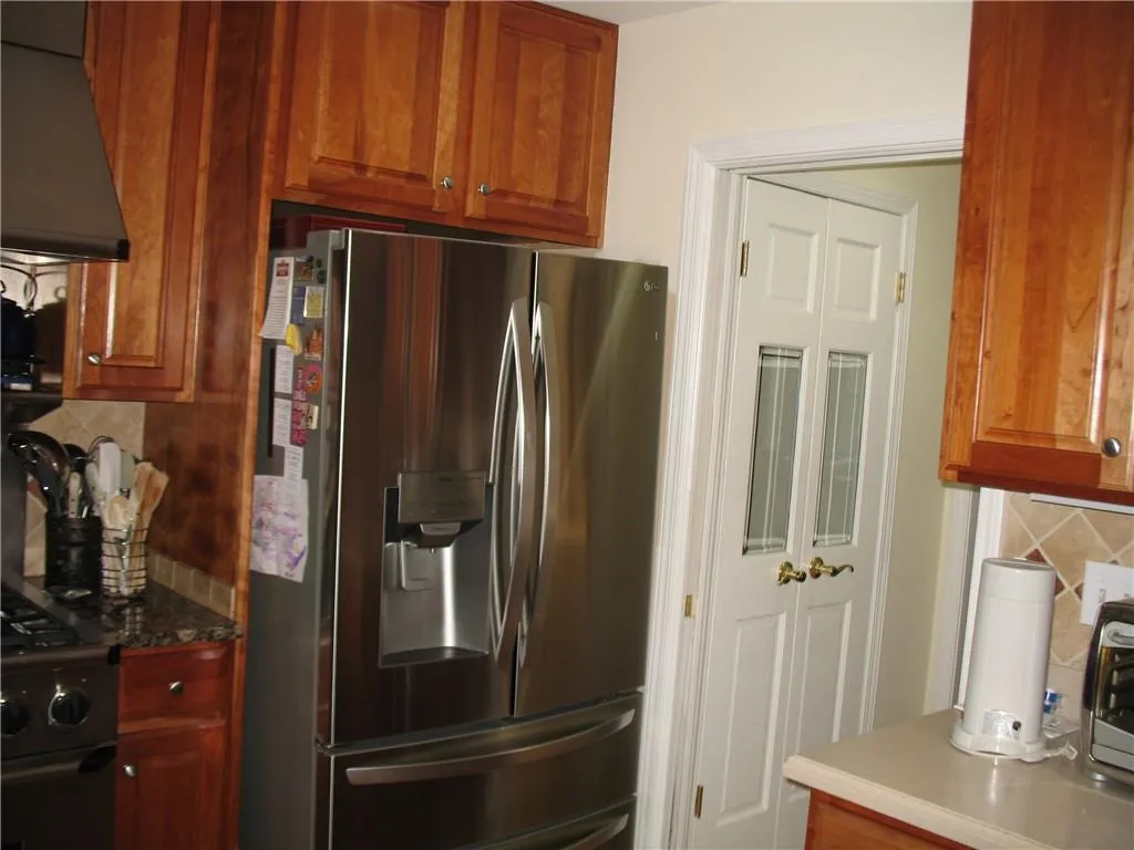 Kitchen with backsplash, stainless steel fridge with ice dispenser, gas range oven, custom exhaust hood, and brown cabinets