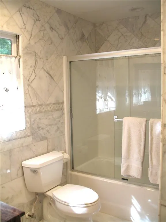 Bathroom featuring tile walls and enclosed tub / shower combo