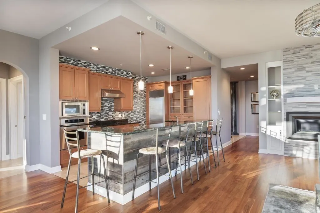 Kitchen with built in appliances, dark stone counters, a kitchen bar, backsplash, and dark wood-type flooring