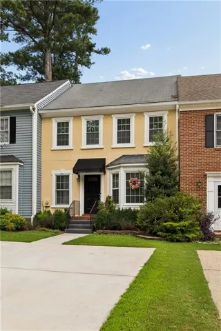 Two-story stucco townhouse with a bay window, black front door, and a coordinating black awning