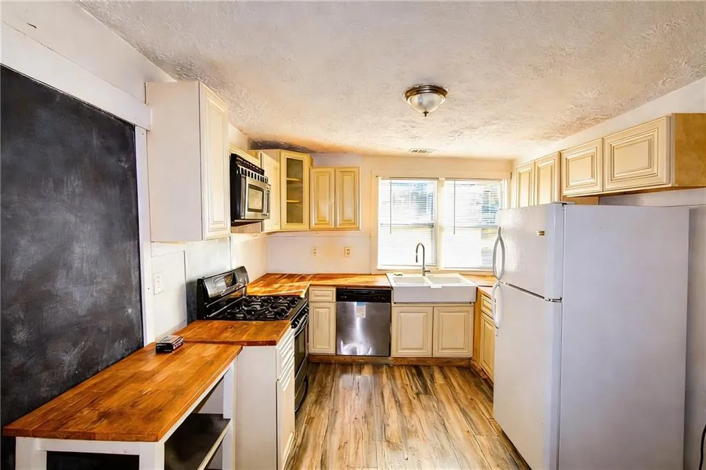 Kitchen with stainless steel appliances, glass insert cabinets, wood counters, a textured ceiling, and light wood-type flooring