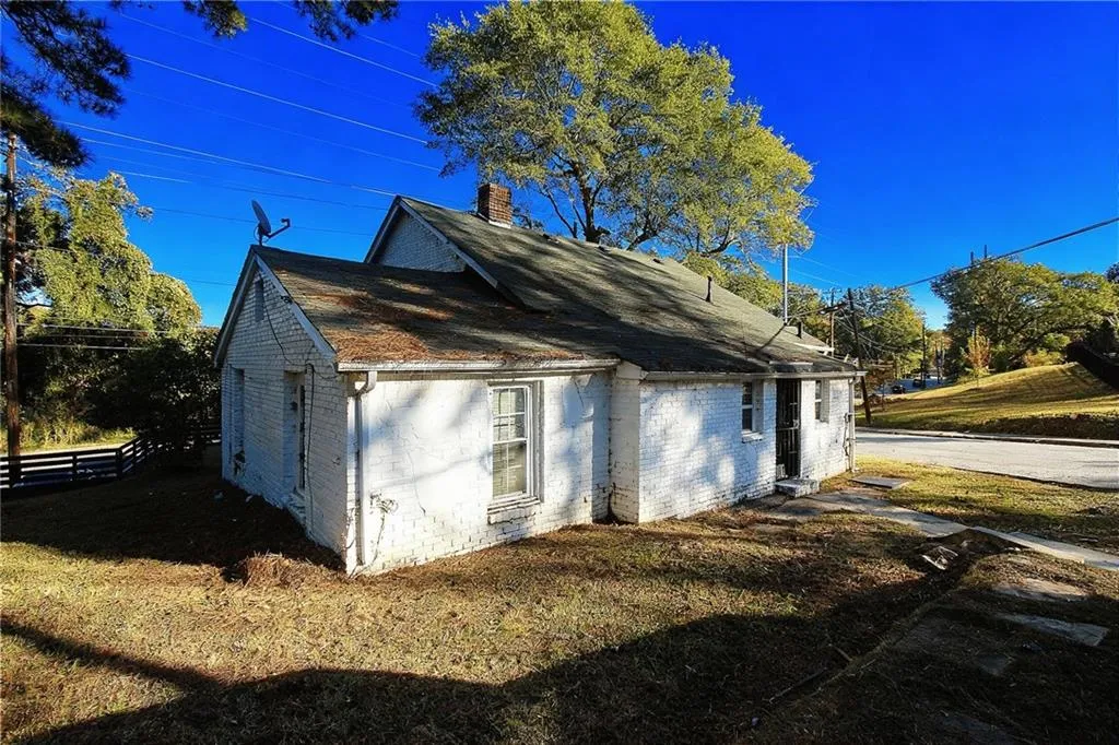 View of side of home with a chimney, roof with shingles, concrete block siding, and a lawn
