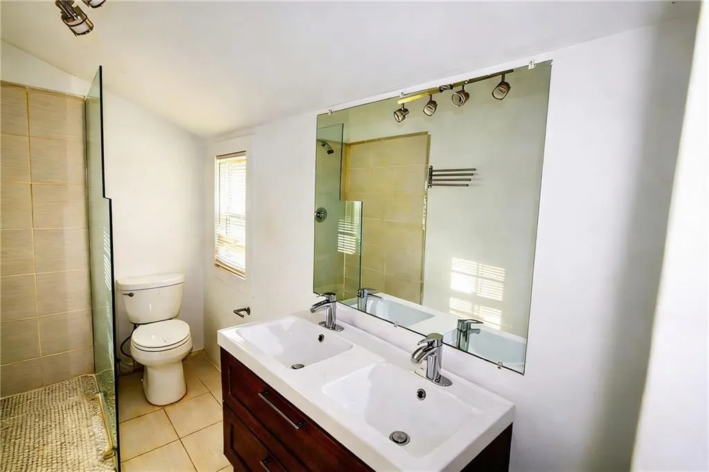 Bathroom featuring double vanity, a tile shower, light tile patterned floors, and vaulted ceiling