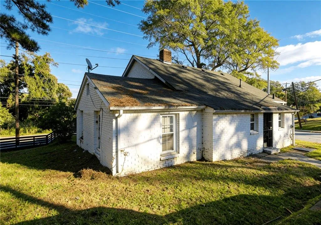 View of property exterior with brick siding, roof with shingles, and a chimney