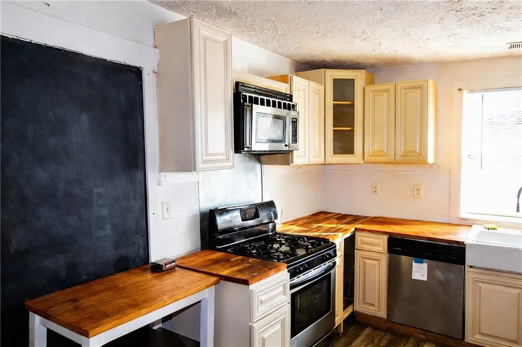 Kitchen with butcher block countertops, stainless steel appliances, glass insert cabinets, dark wood-type flooring, and a textured ceiling