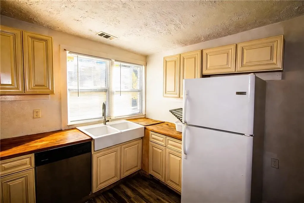Kitchen featuring freestanding refrigerator, stainless steel dishwasher, butcher block counters, and dark wood-style floors