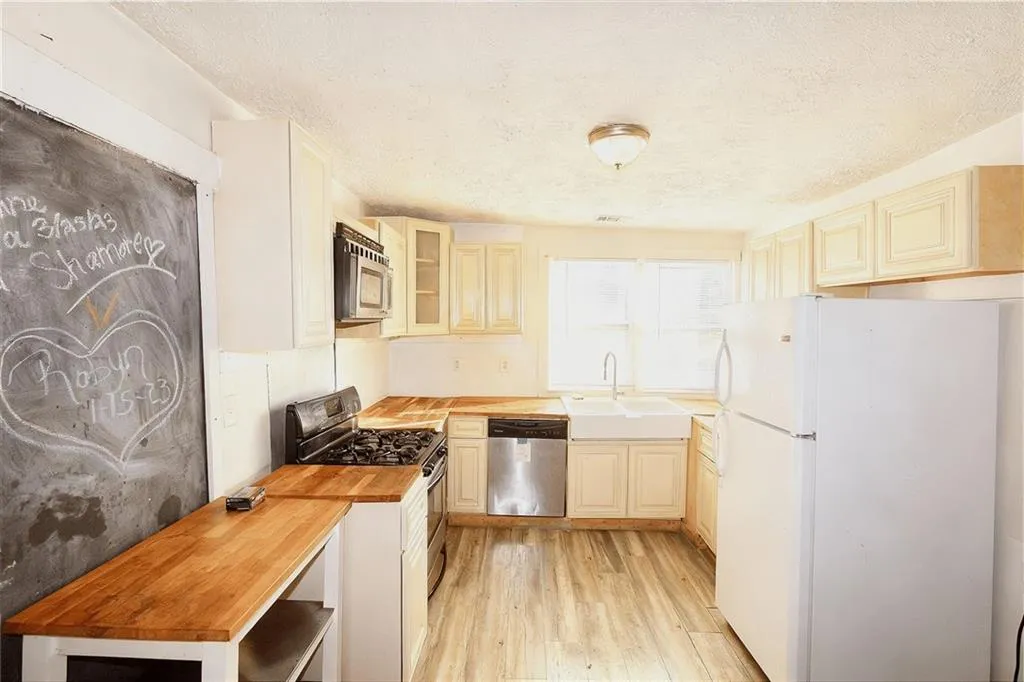Kitchen with wood counters, stainless steel appliances, glass insert cabinets, a textured ceiling, and light wood-style flooring