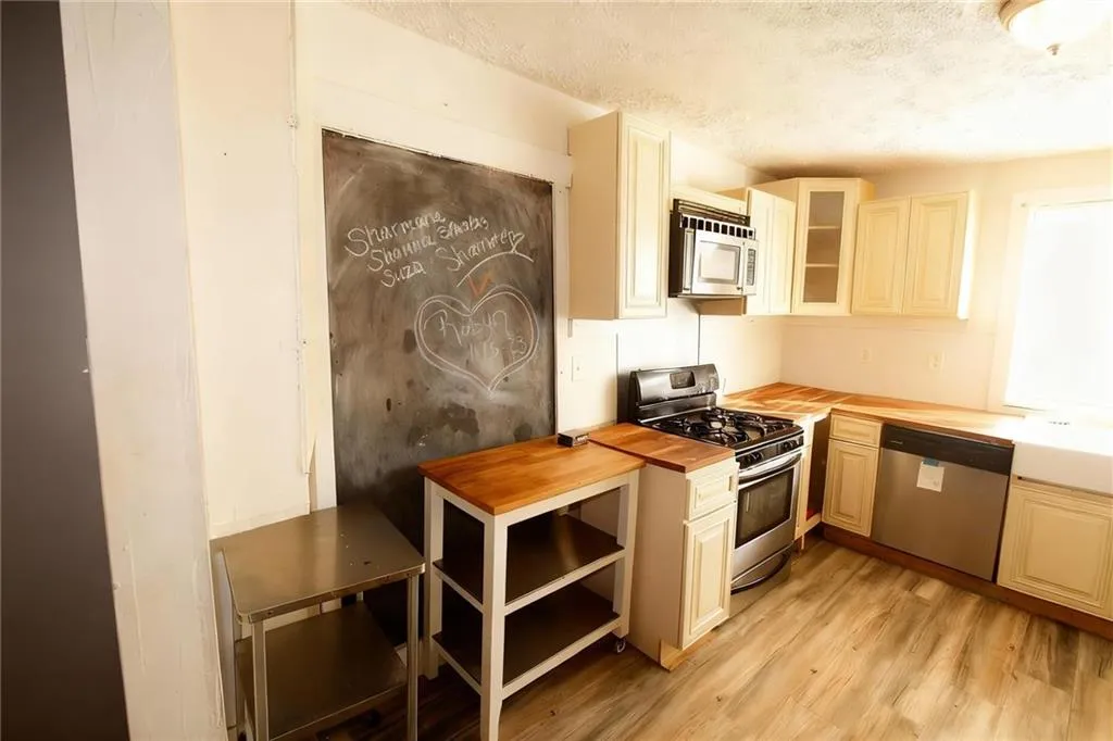 Kitchen with appliances with stainless steel finishes, glass insert cabinets, light wood-style floors, a textured ceiling, and butcher block countertops