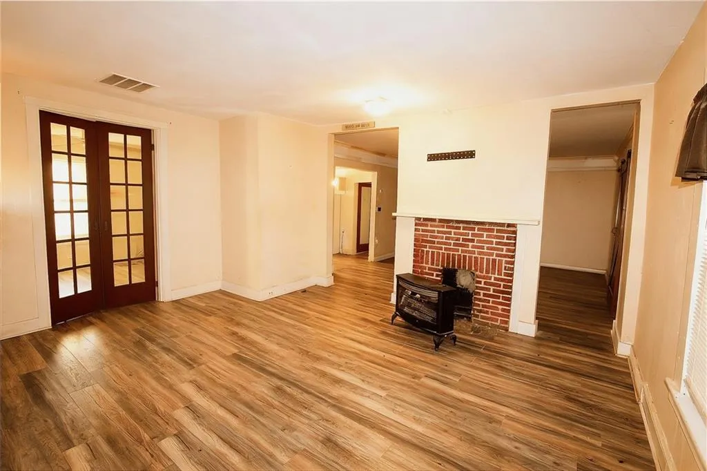 Unfurnished living room featuring a wood stove, wood finished floors, and french doors