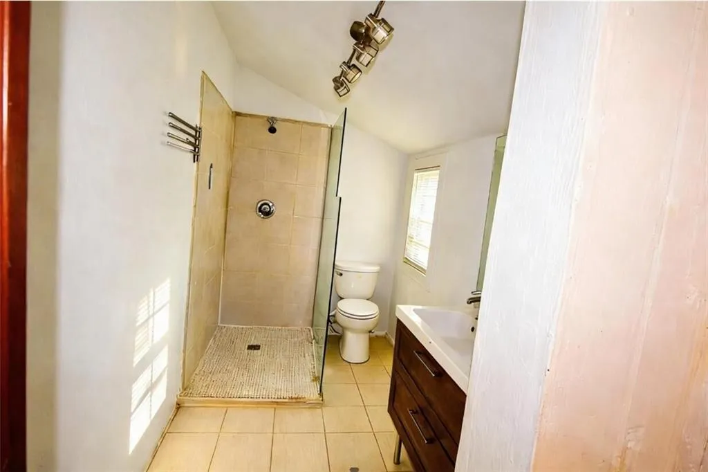 Bathroom featuring a shower stall, vanity, light tile patterned floors, and lofted ceiling