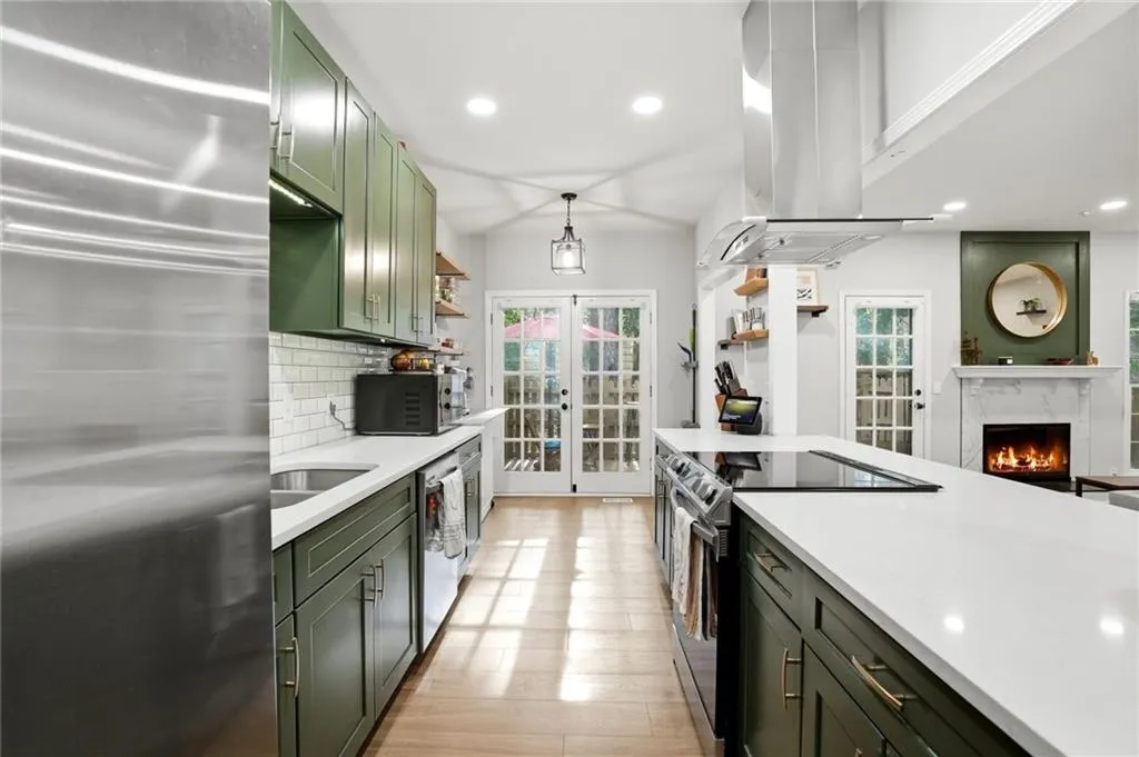 Kitchen with french doors, stainless steel appliances, a high end fireplace, island exhaust hood, and light wood-style floors