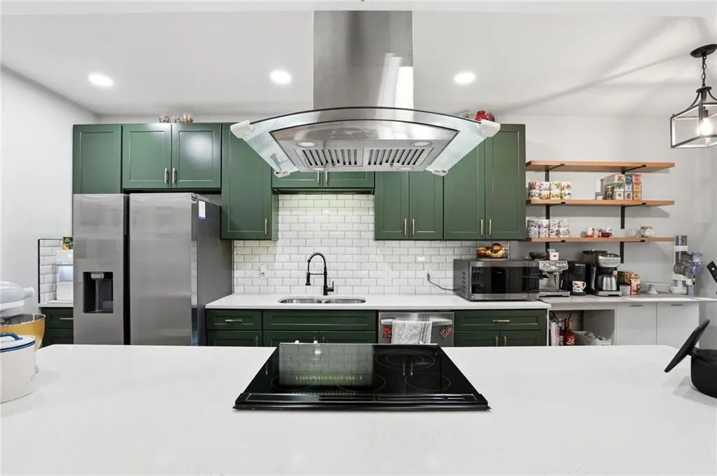 Kitchen featuring green cabinets, island exhaust hood, stainless steel appliances, and light stone counters