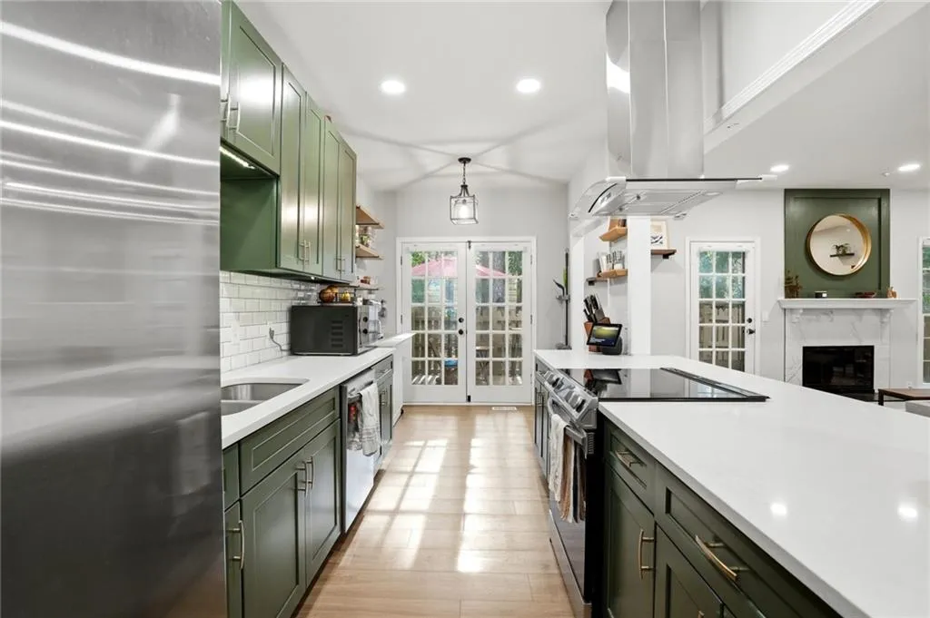 Kitchen featuring green cabinets, french doors, black appliances, a high end fireplace, and island exhaust hood