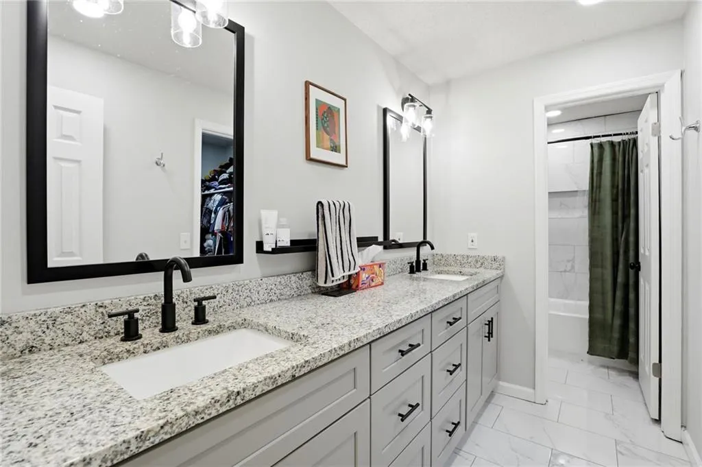 Full bath featuring double vanity, shower / tub combo, light marble finish flooring, and a walk in closet