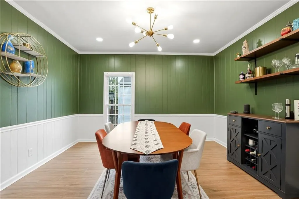 Dining space with suspended lighting, ornamental molding, light wood-style flooring, and wood walls