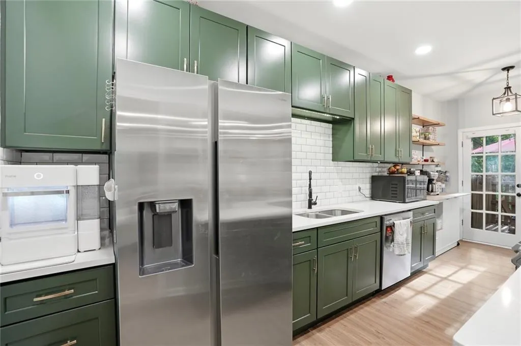 Kitchen with green cabinetry, stainless steel appliances, light wood-style floors, tasteful backsplash, and light stone counters
