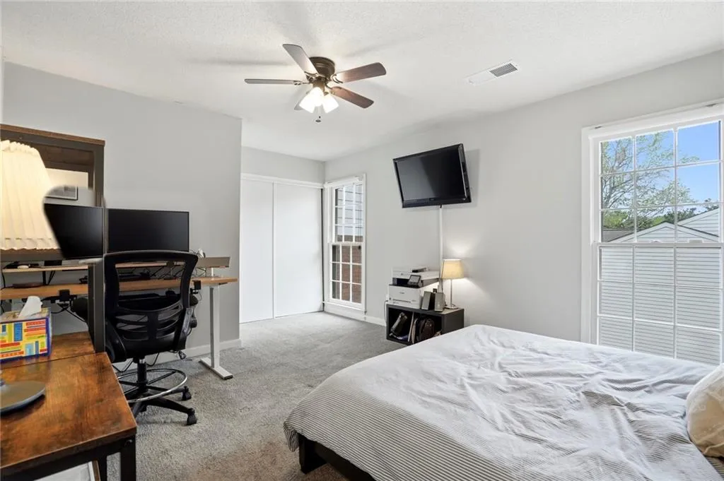 Bedroom featuring a desk, light colored carpet, a textured ceiling, multiple windows, and ceiling fan