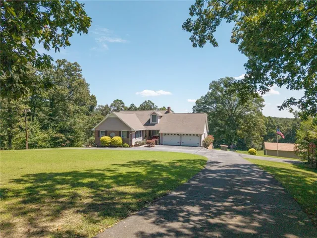 Expansive green lawn with mature trees, a paved driveway, and a detached structure