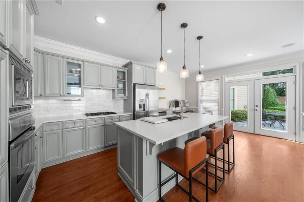 Kitchen featuring appliances with stainless steel finishes, gray cabinetry, a kitchen breakfast bar, backsplash, and light countertops