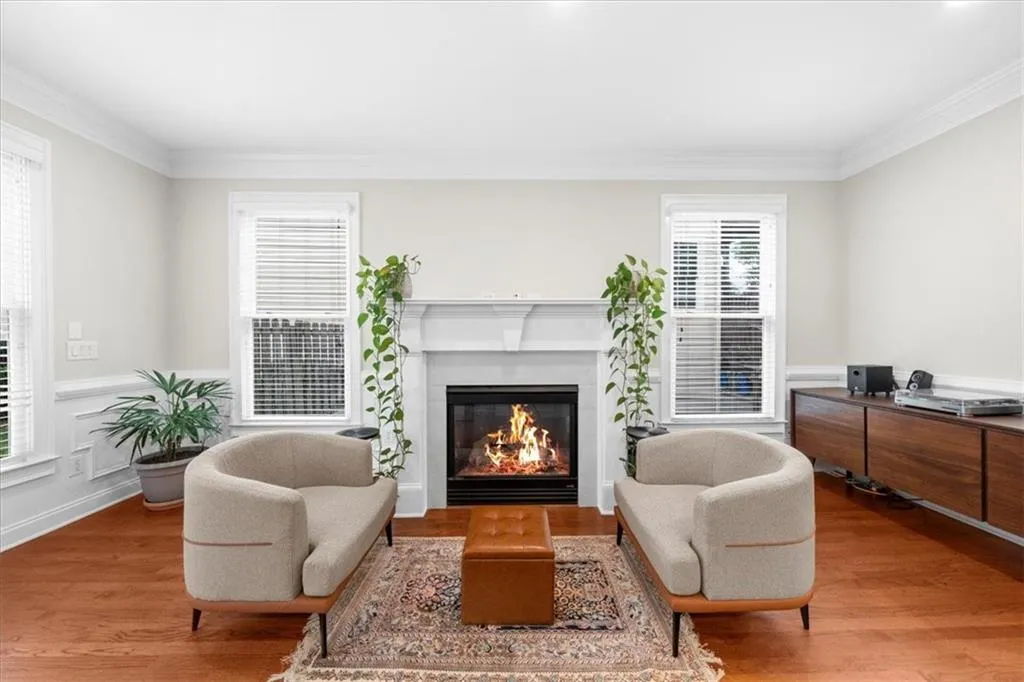 Living area featuring wood finished floors, a glass covered fireplace, ornamental molding, and a wainscoted wall