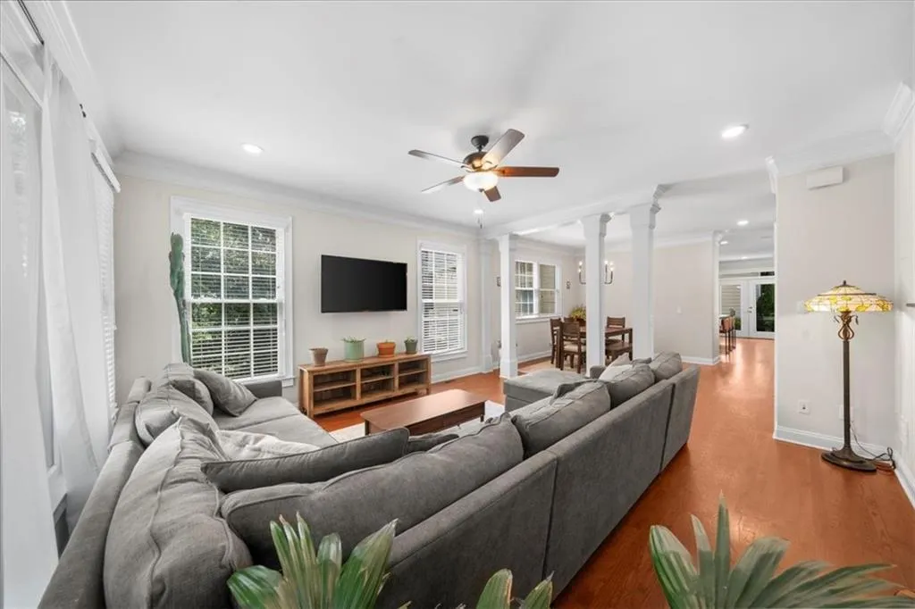 Living room featuring a ceiling fan, ornamental molding, recessed lighting, wood finished floors, and ornate columns