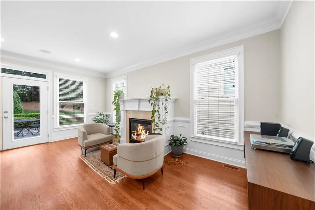 Sitting room featuring crown molding, a glass covered fireplace, wood finished floors, recessed lighting, and a wainscoted wall