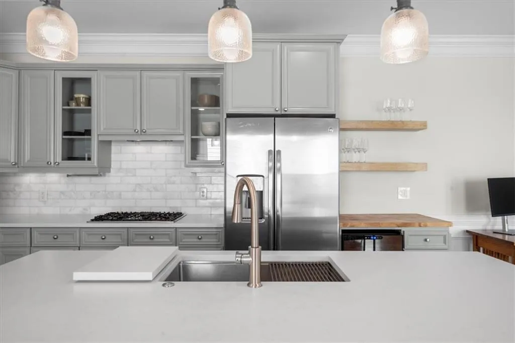 Kitchen with appliances with stainless steel finishes, gray cabinets, light countertops, hanging light fixtures, and ornamental molding